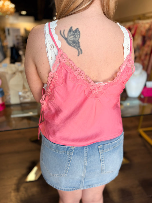 Person wearing a pink lace top and denim skirt with a tattoo on the back in an indoor setting.