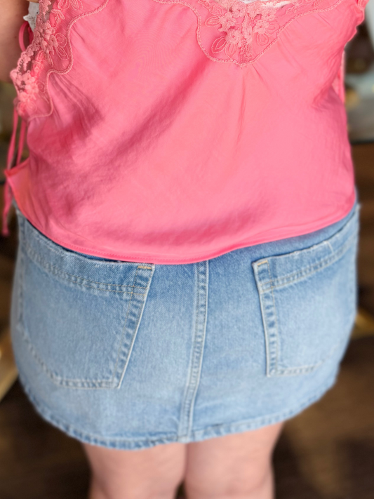 Person wearing a pink lace top and denim skirt with a tattoo on the back in an indoor setting.
