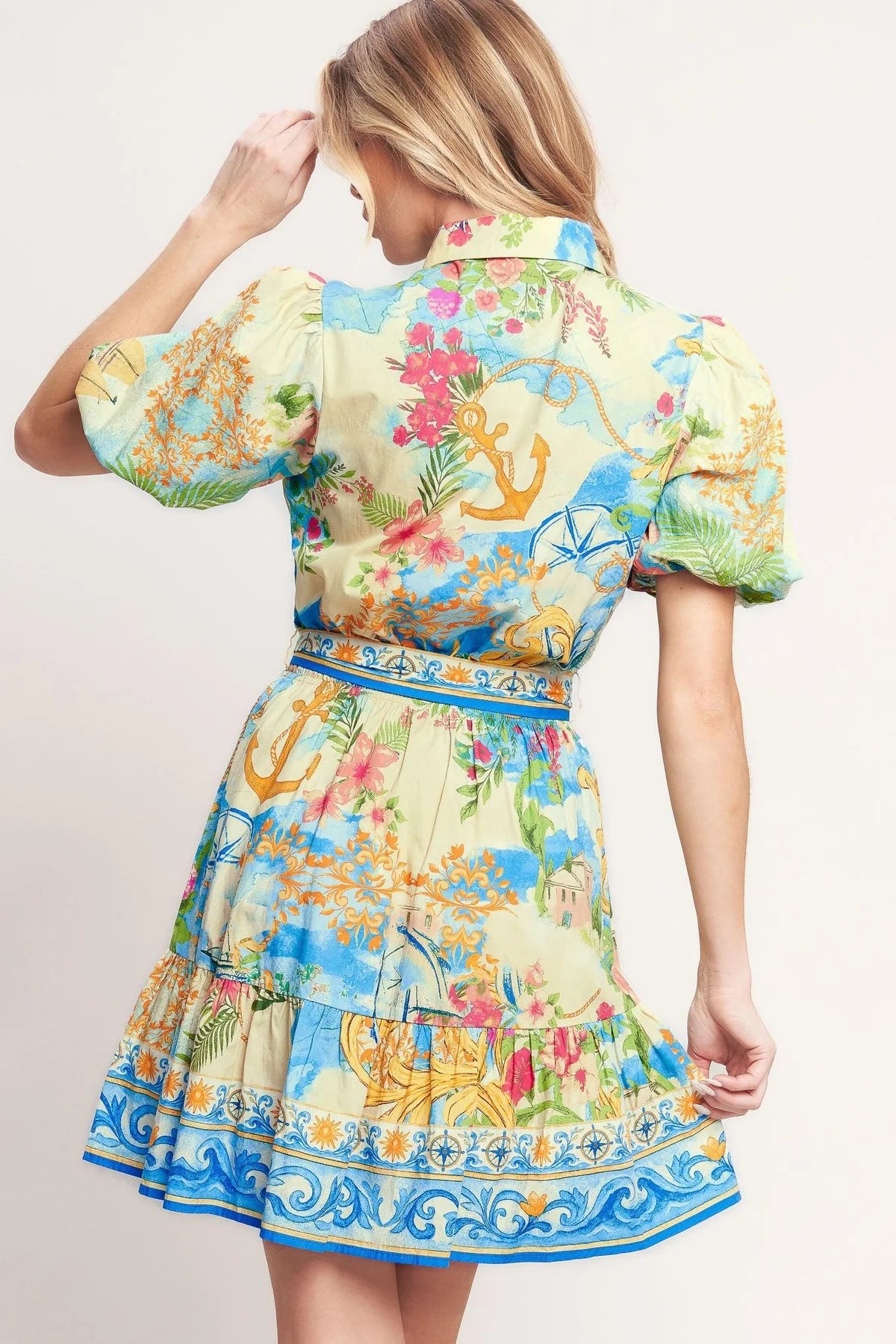 Woman wearing a colorful dress with floral and anchor patterns on a plain background