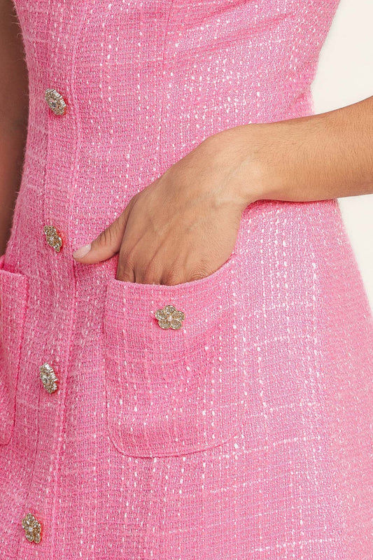 Close-up of a pink garment with decorative buttons and a hand in the pocket.