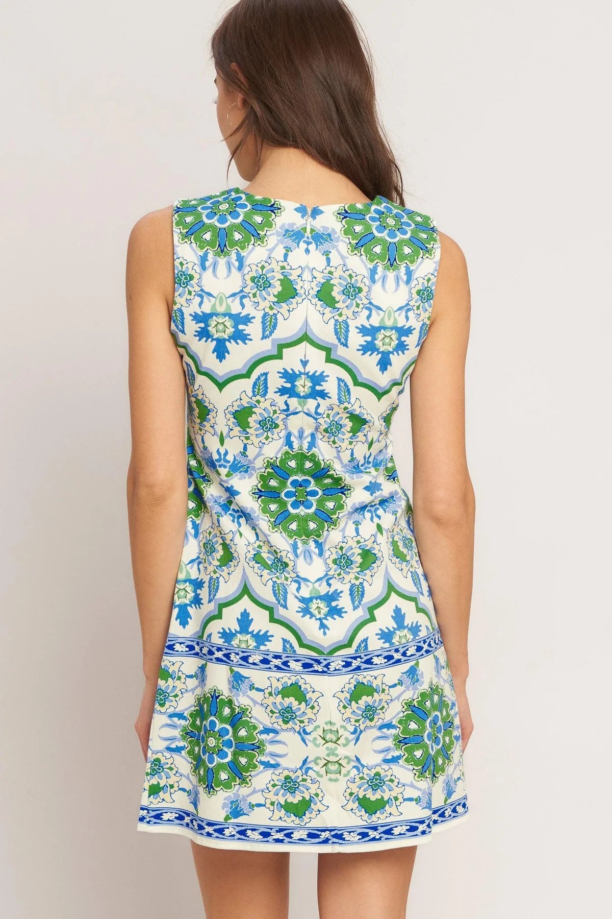 Woman wearing a sleeveless dress with a colorful geometric pattern on a plain background