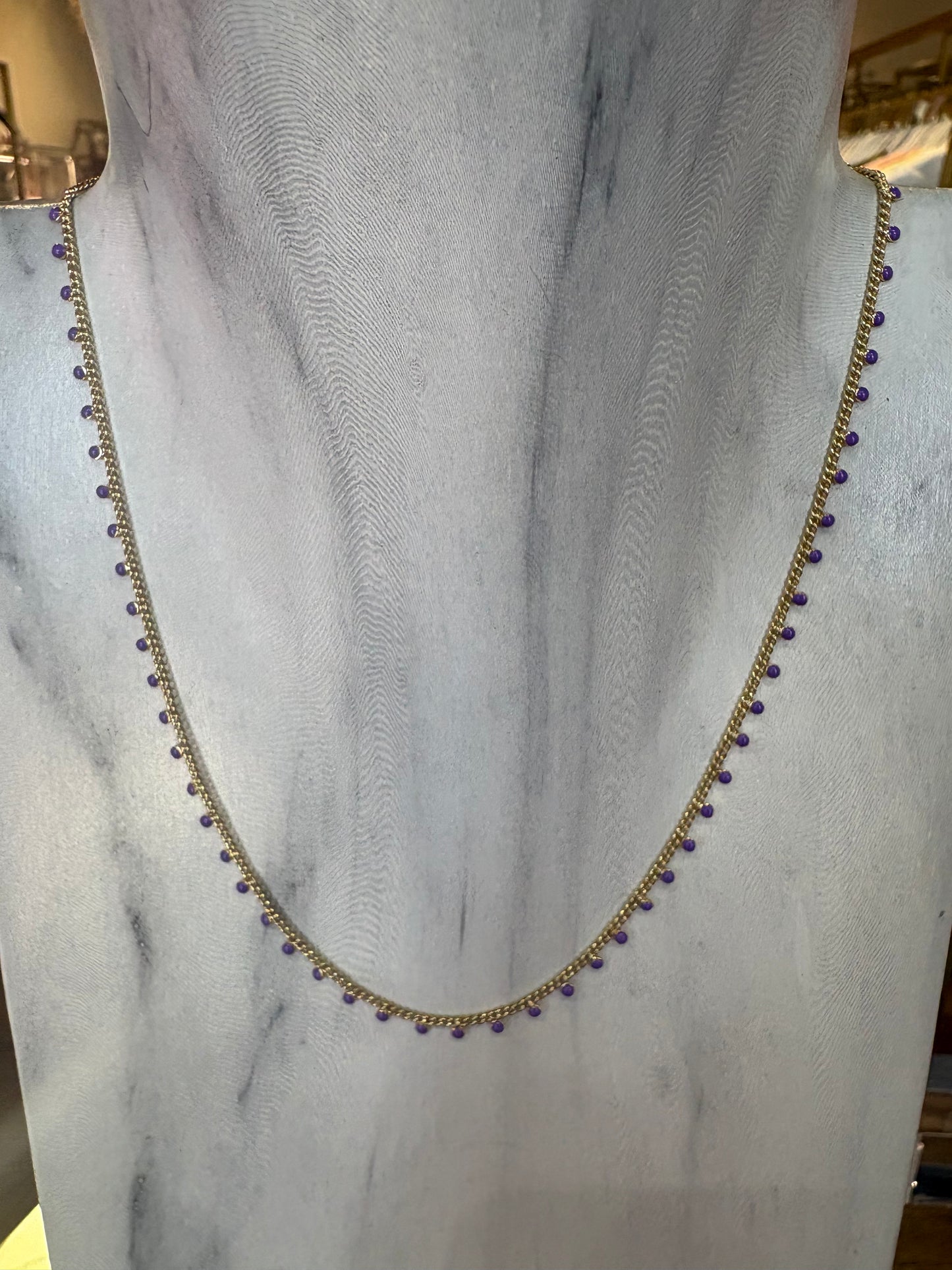 Gold KENDRA SCOTT necklace with purple beads on a marble surface.