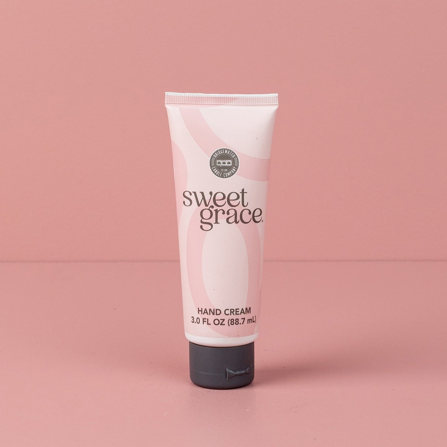 A tube of SWEET GRACE hand cream against a pink background.