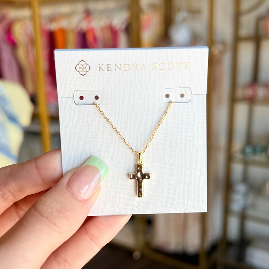 Gold necklace on a Kendra Scott card held by a hand with a blurred store background