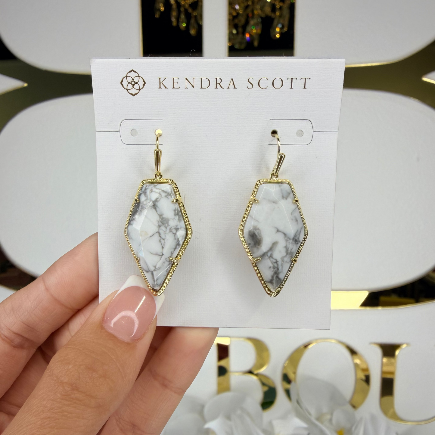 Kendra Scott earrings on a card held by a hand with a blurred background