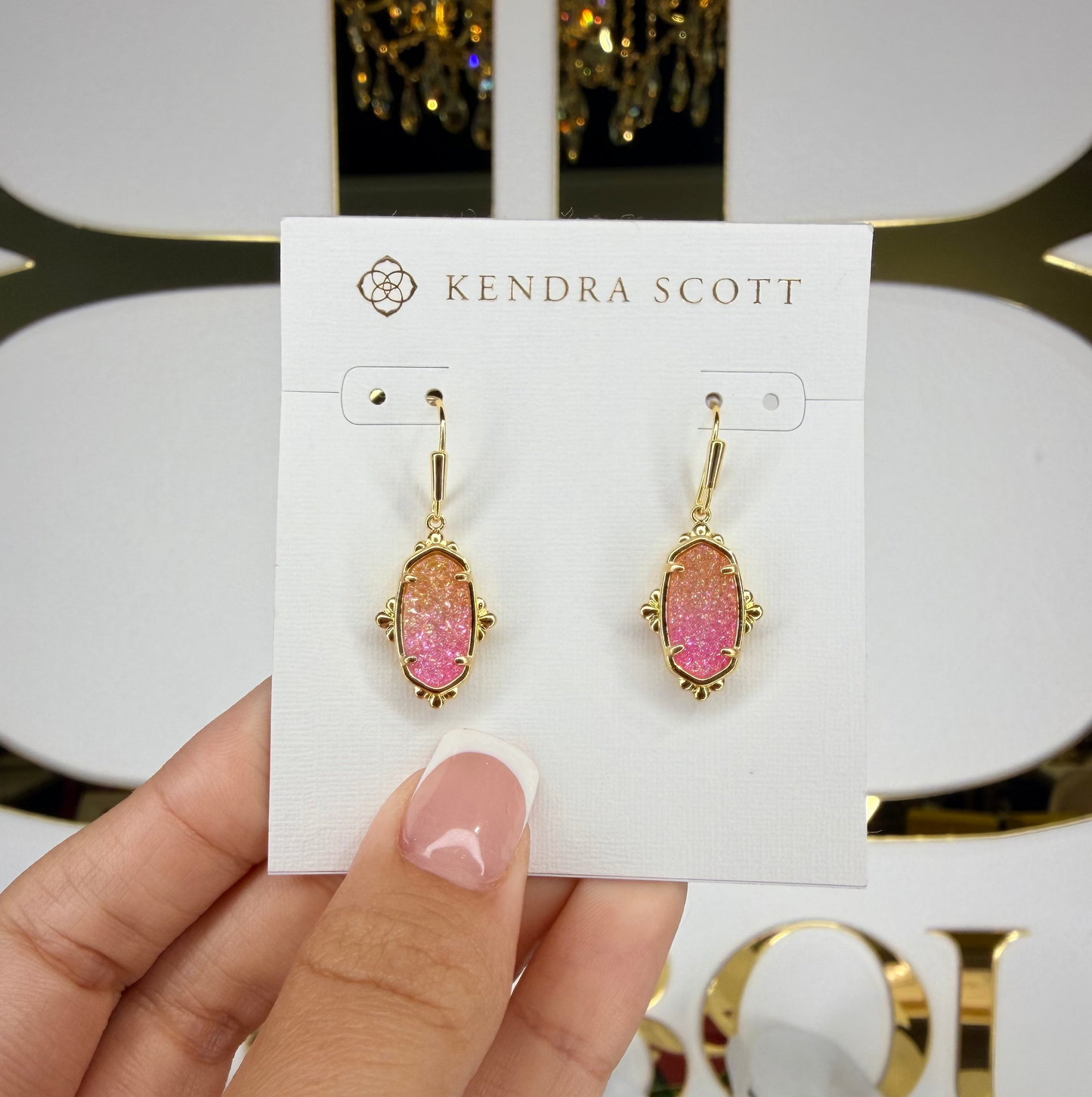 Kendra Scott earrings on a card held by a hand with a decorative background