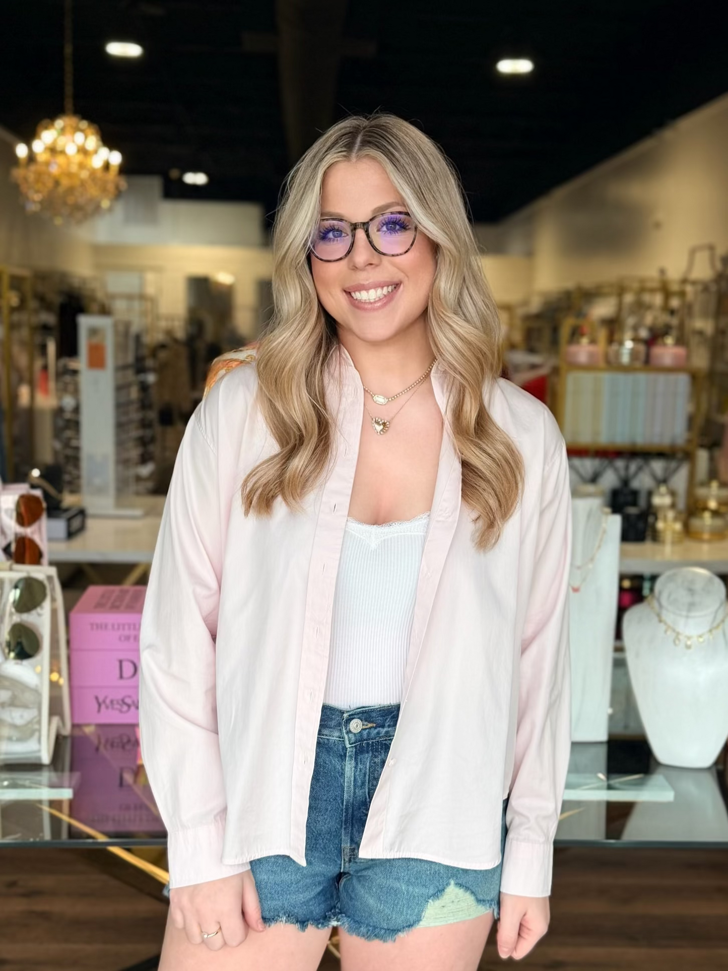Model wearing Pink button up top with white lace tank and blue denim shorts