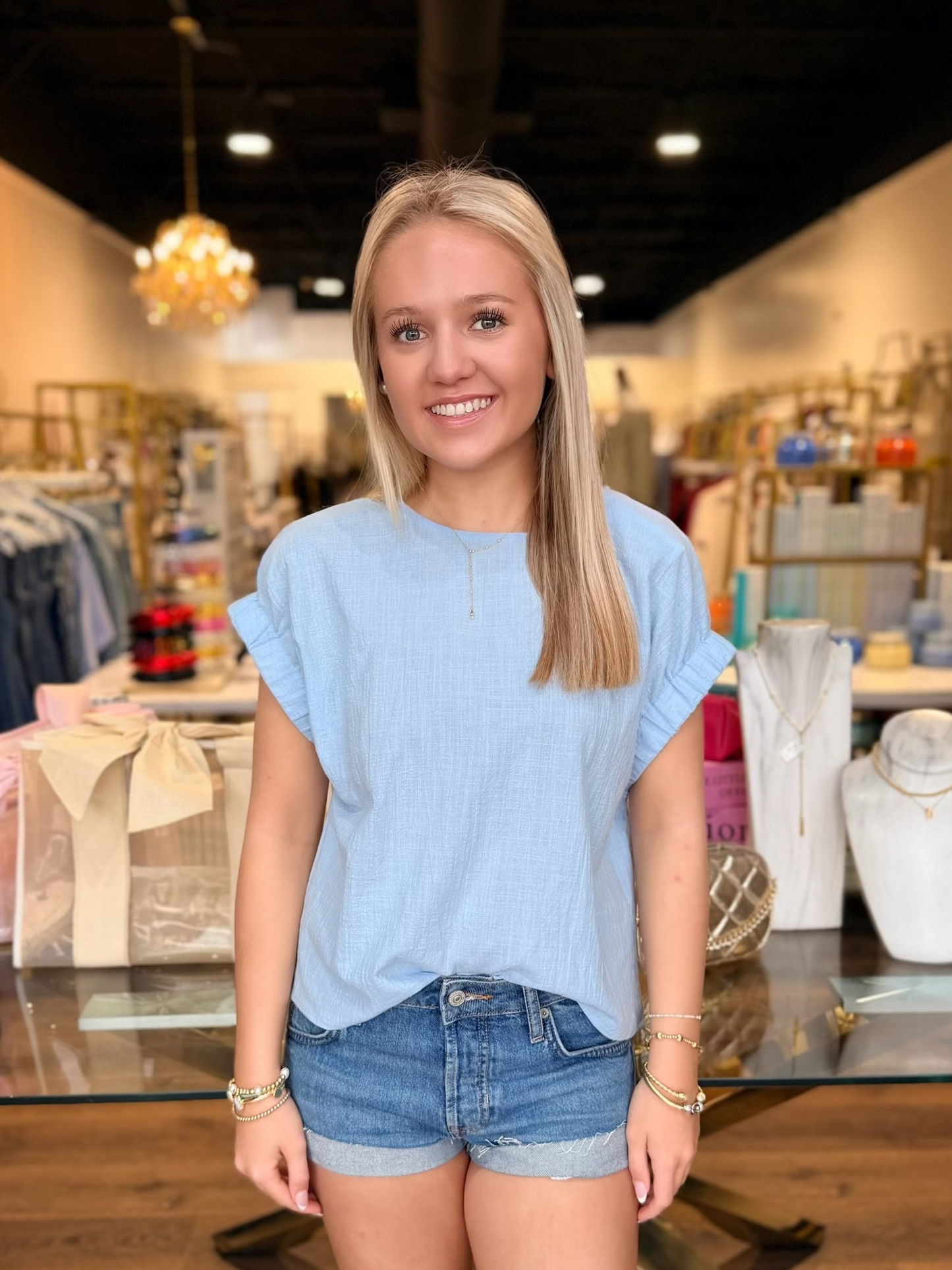 Woman in a light blue top and denim shorts standing in a store.