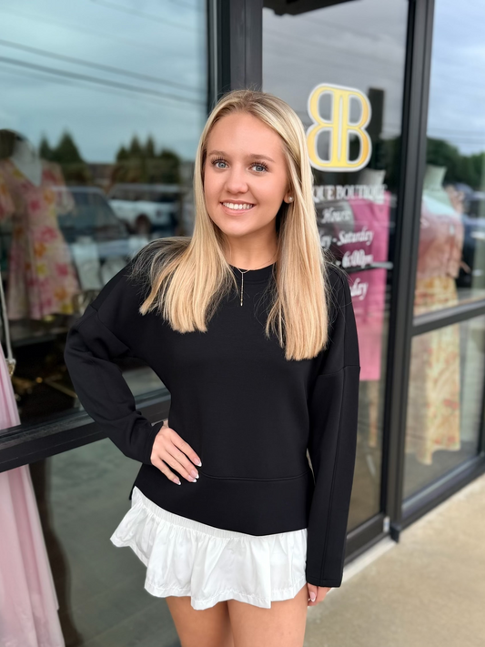 Woman wearing a black sweater and white skirt standing in front of a store window.