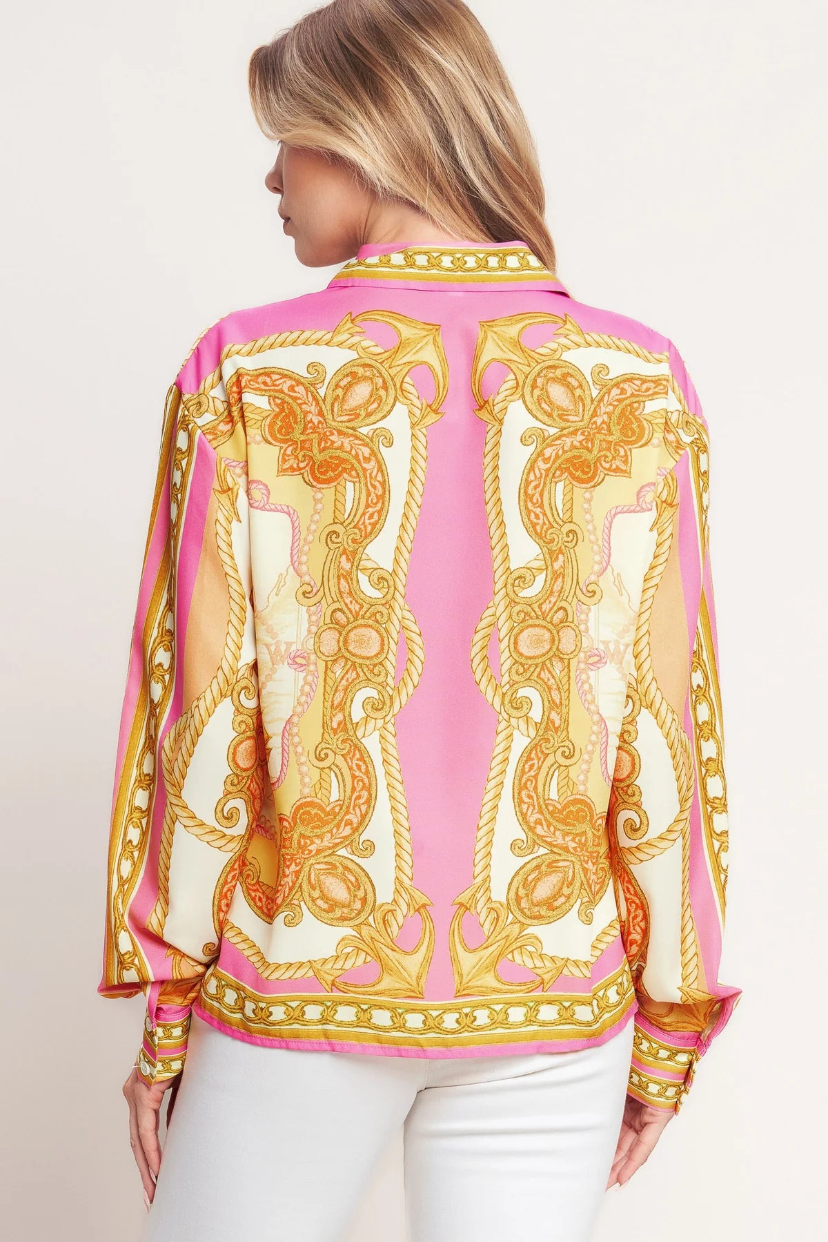 Woman wearing a pink and gold patterned blouse with white pants on a plain background