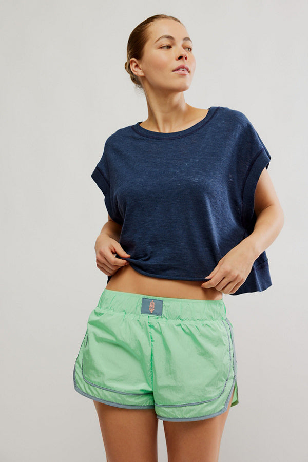 Woman wearing a blue oversized shirt and green shorts on a plain background