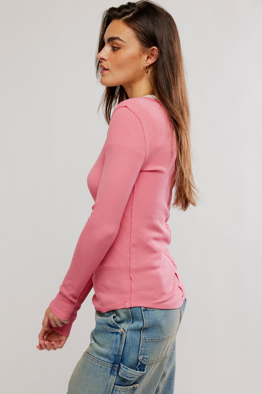 Woman wearing a pink long-sleeve top and blue jeans on a plain background