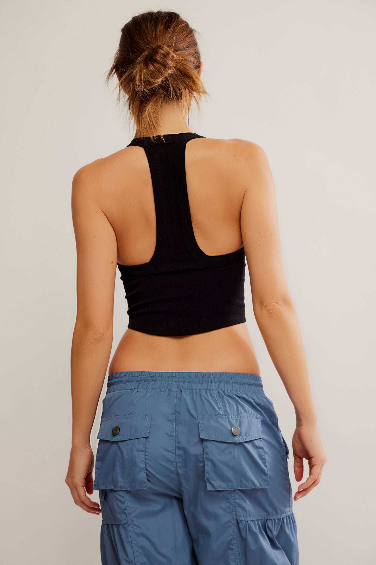 Person wearing a black crop top and blue cargo pants on a plain background