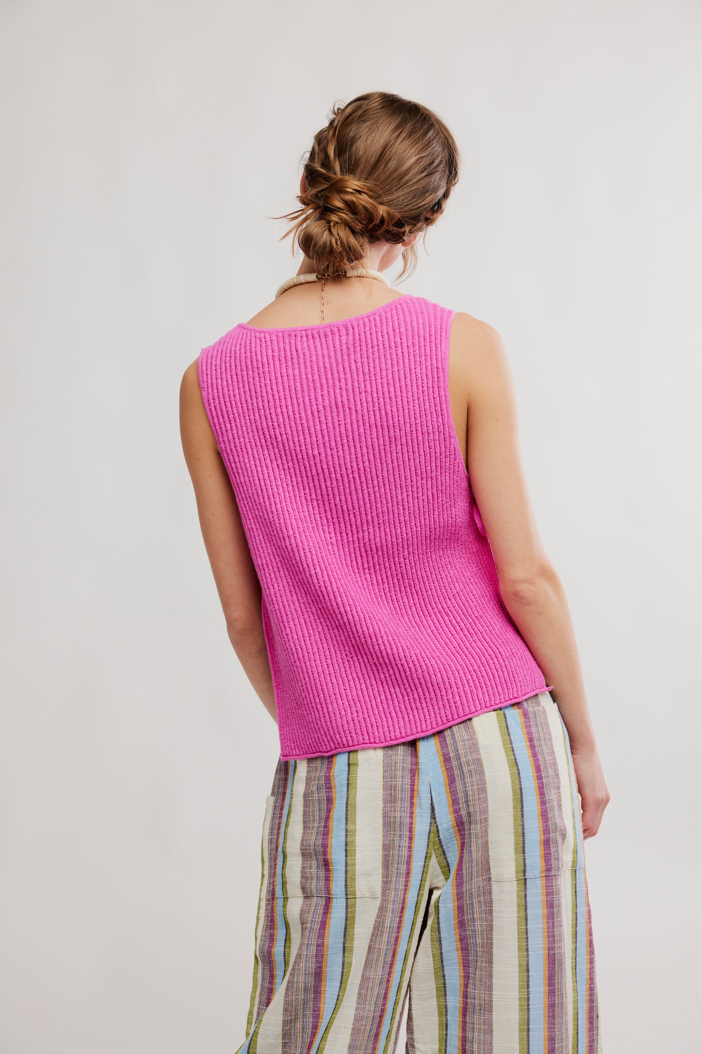 Person wearing a bright pink sleeveless top and colorful striped pants on a plain background