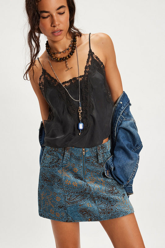 Woman wearing a black lace top and blue paisley skirt with a denim jacket on a white background