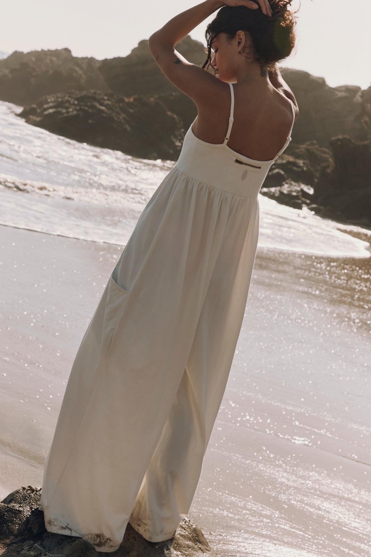 Woman in a white dress standing on a rocky beach with ocean waves in the background