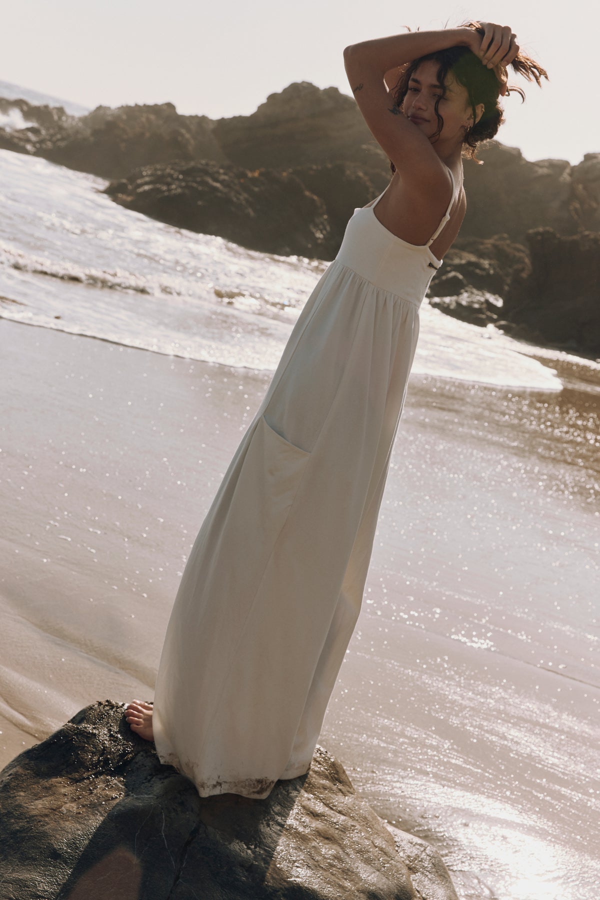 Woman in a white dress standing on a rocky beach with waves in the background