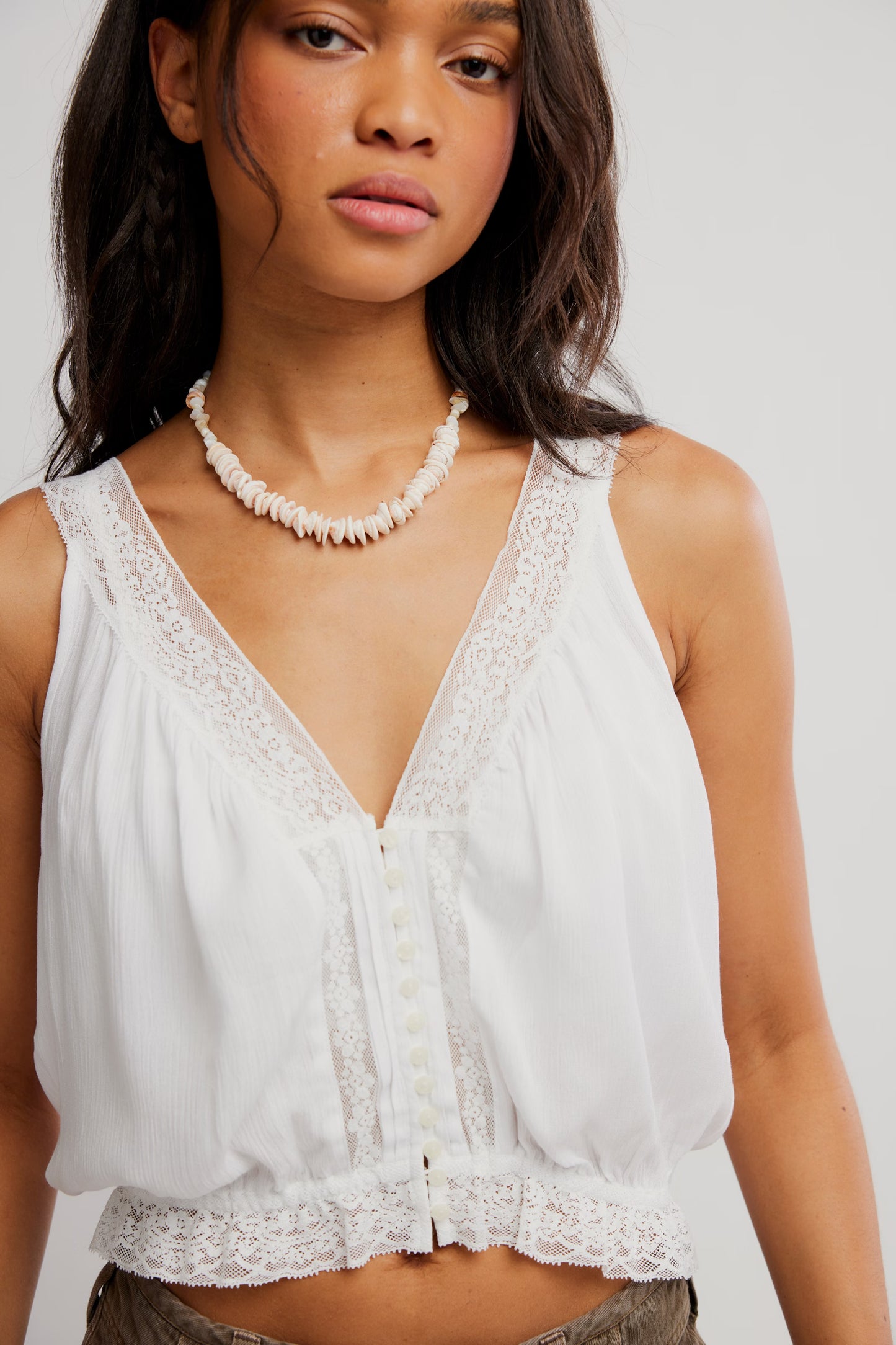 Woman wearing a white lace top and pearl necklace on a plain background