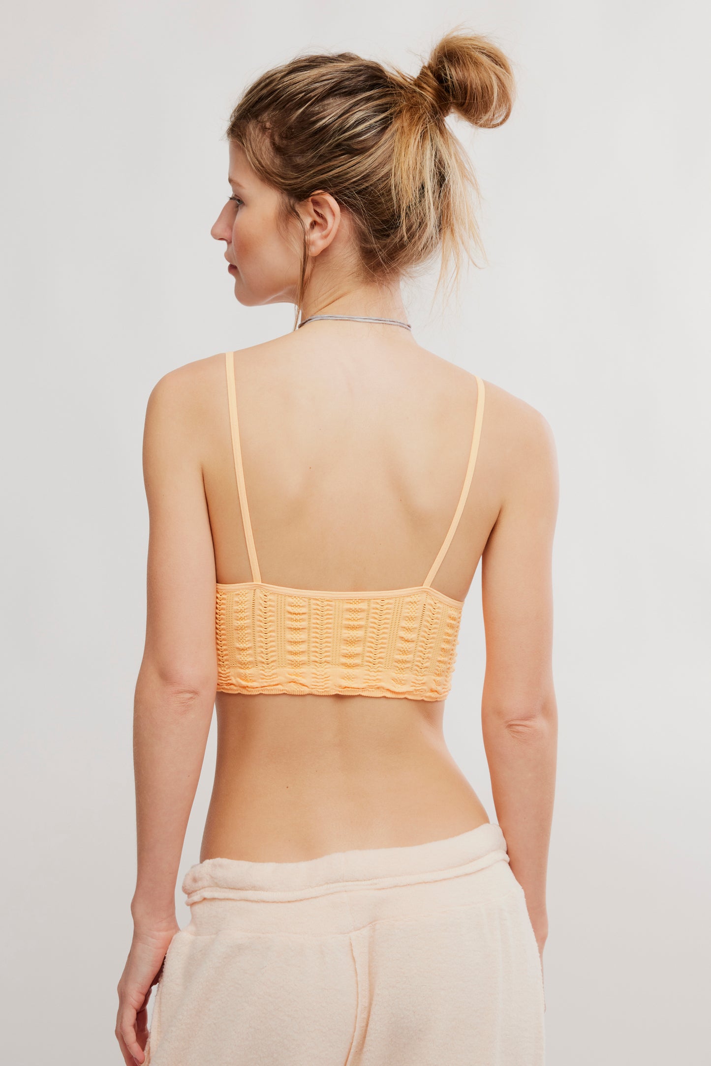 Woman wearing a yellow crochet top against a plain background