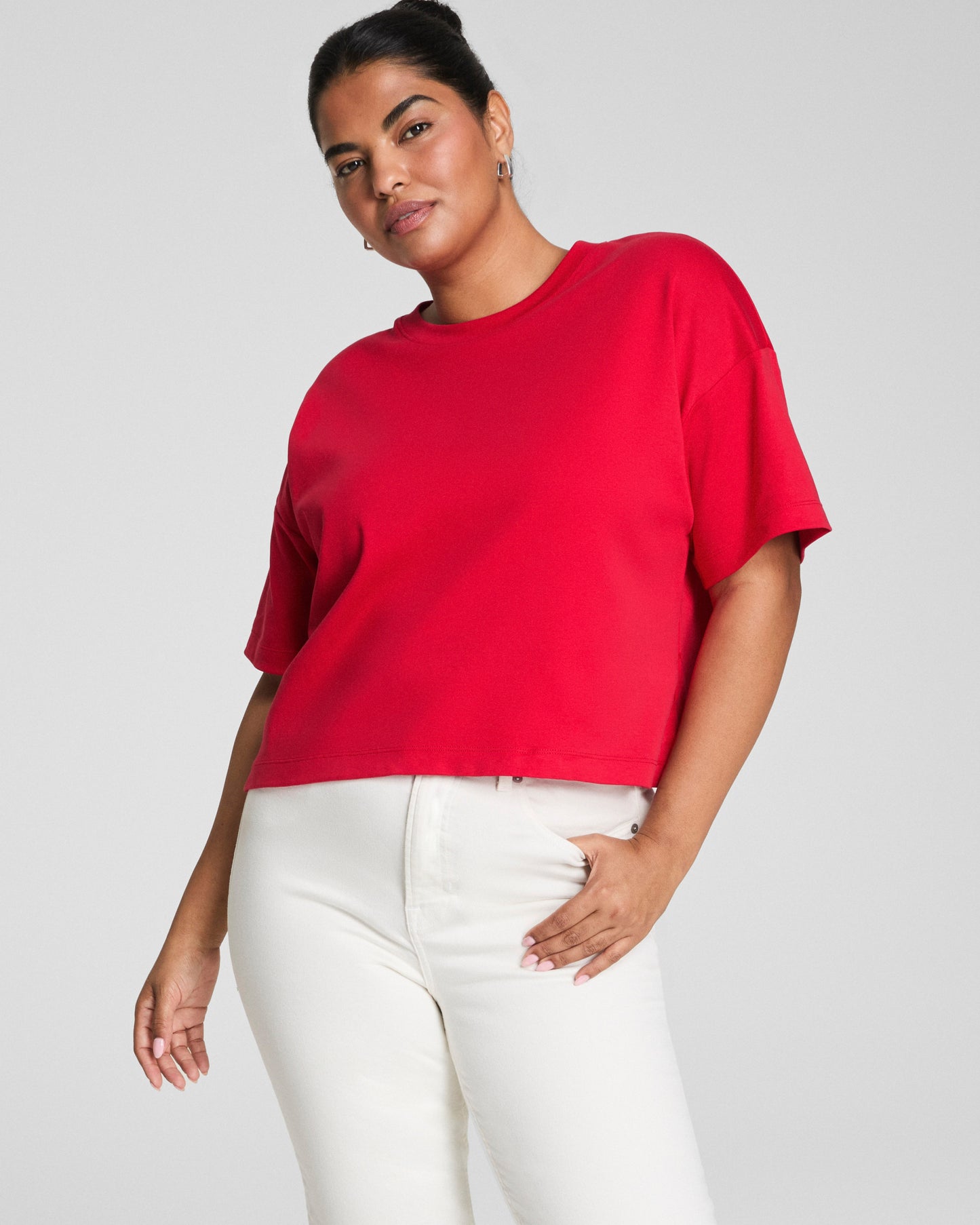 Person wearing a red SPANX t-shirt and white pants on a plain background