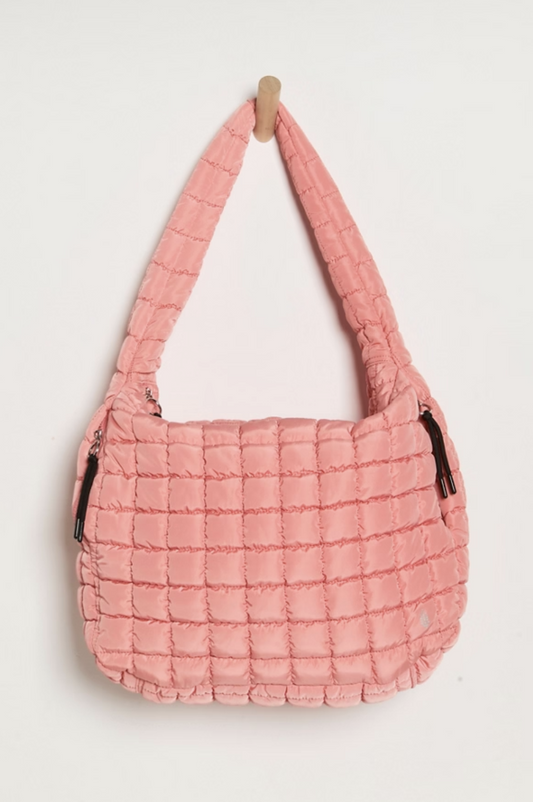 A pink quilted shoulder bag with a thick strap, hanging from a small wooden hanger against a plain white background.