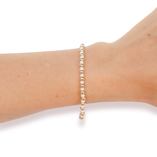 A delicate beaded bracelet with small white pearls and gold spacer beads, shown worn on a person's wrist against a plain white background.