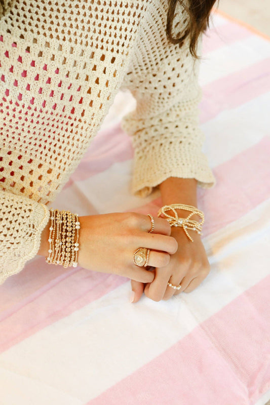 Close-up of hands wearing gold jewelry on a pink and white striped fabric background