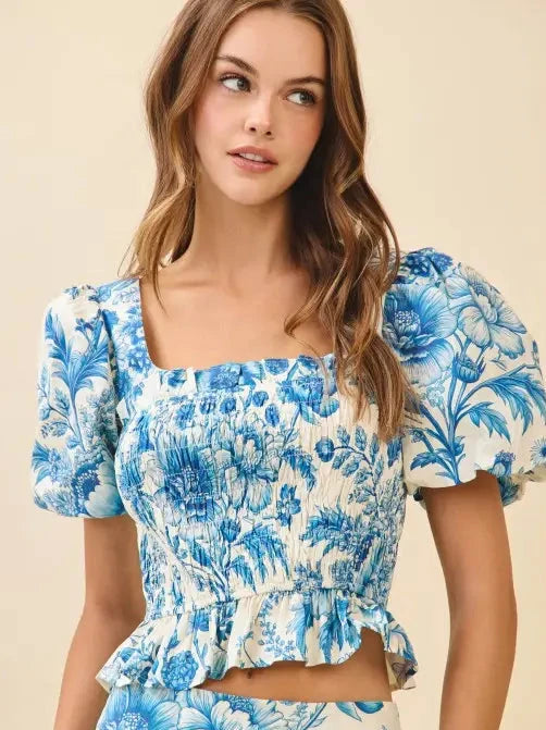 Woman wearing a blue floral top with puff sleeves on a beige background