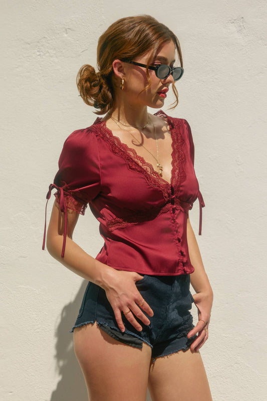 Woman wearing a red blouse and denim shorts against a light background