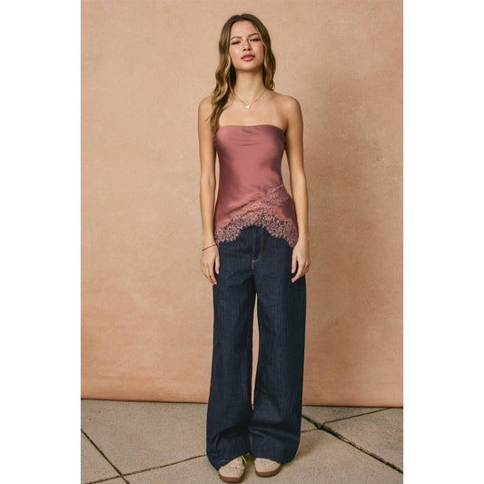 Woman wearing a strapless top and wide-leg jeans against a beige wall.