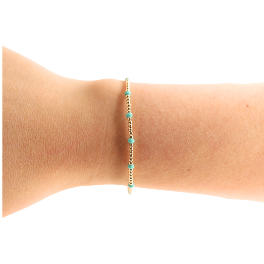 Gold and turquoise beaded bracelet on a wrist against a white background