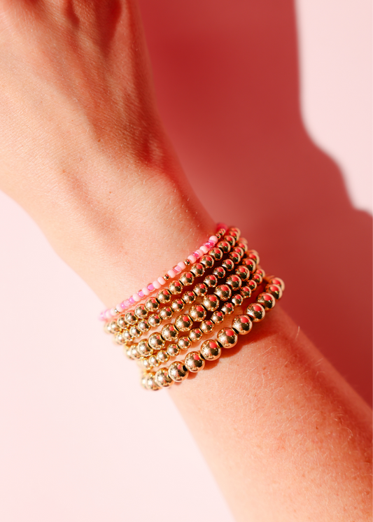 Gold beaded bracelet on a wrist with a pink background