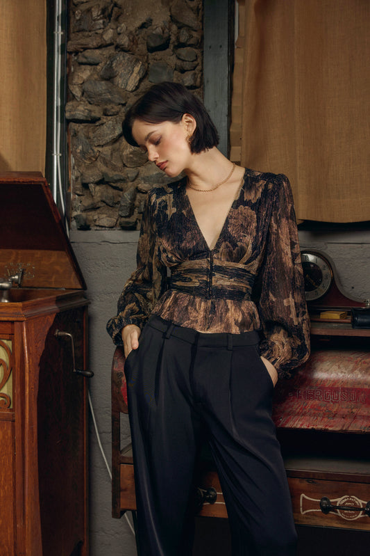 Woman in a patterned blouse and dark pants sitting in a room with vintage furniture.