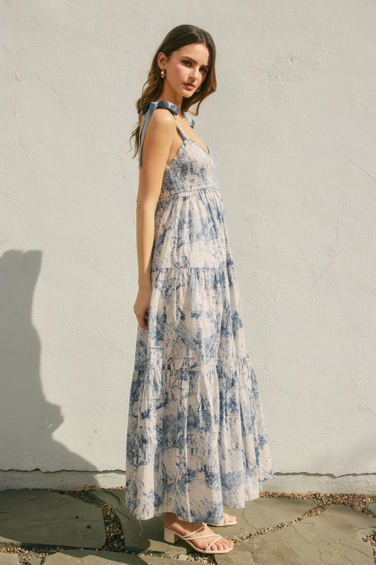 Woman wearing a blue and white floral dress against a plain wall.