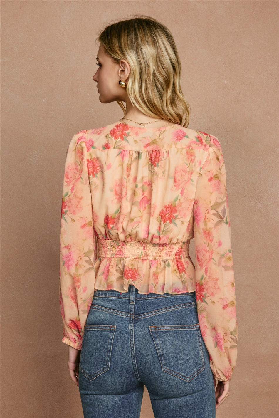 Woman wearing a floral blouse and jeans against a beige background