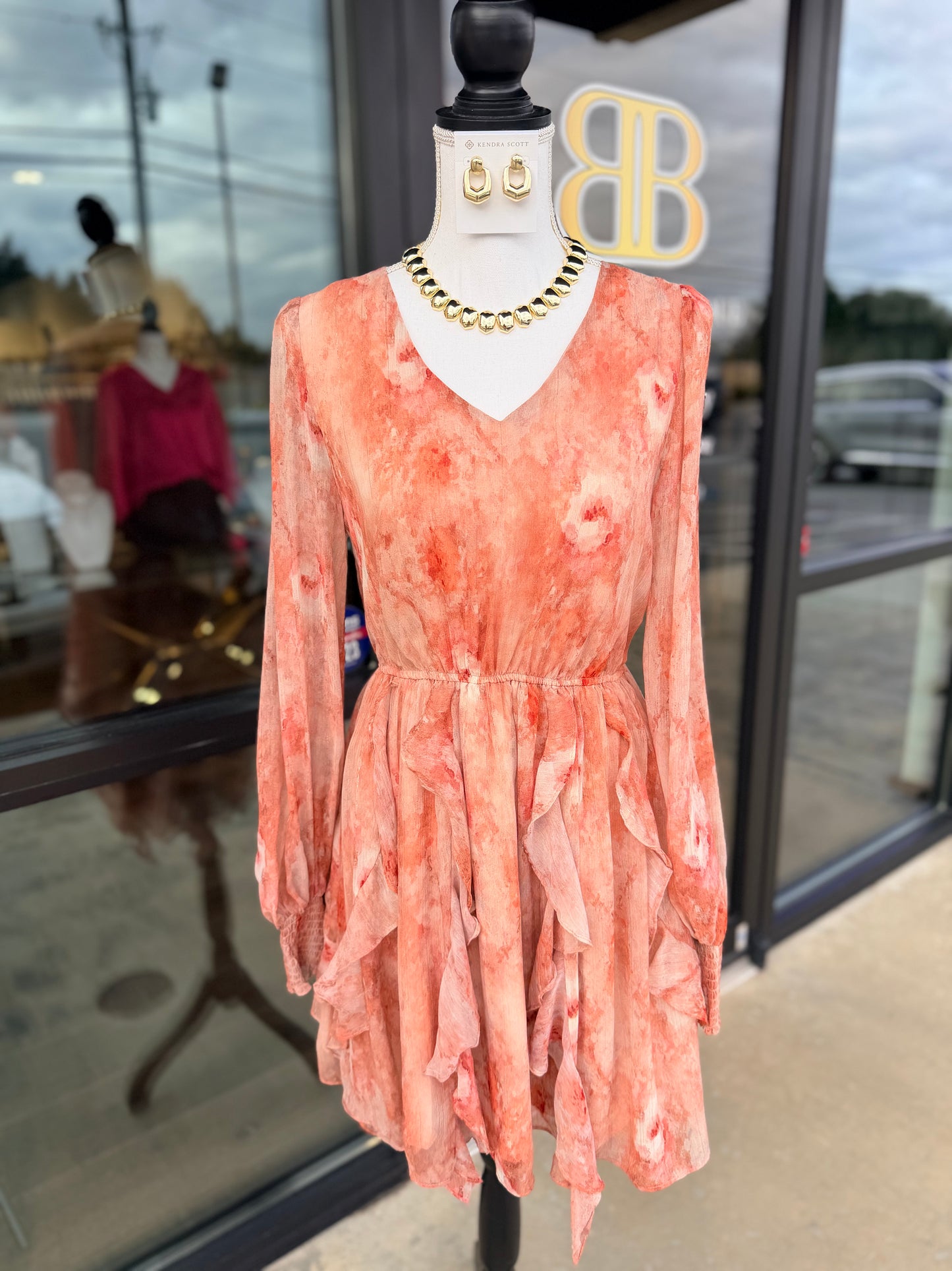 Mannequin wearing a pink floral dress with gold jewelry in a store setting.