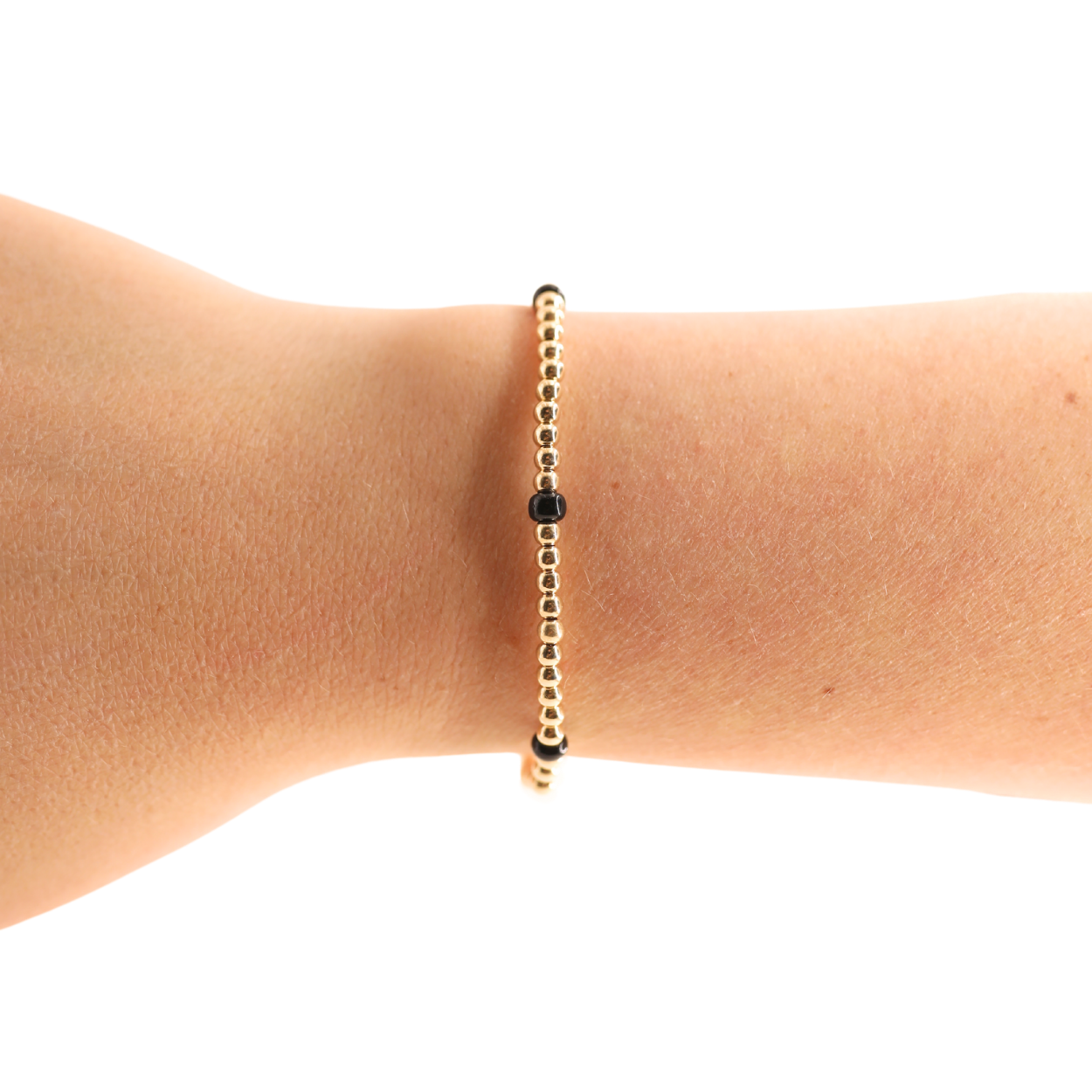 A delicate gold beaded bracelet with a central black bead, shown worn on a person's wrist against a plain white background.