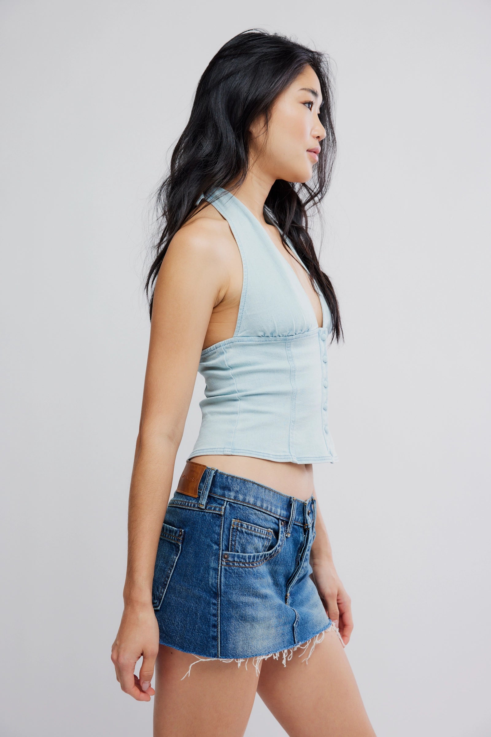 Woman wearing a light blue sleeveless top and denim shorts on a plain background