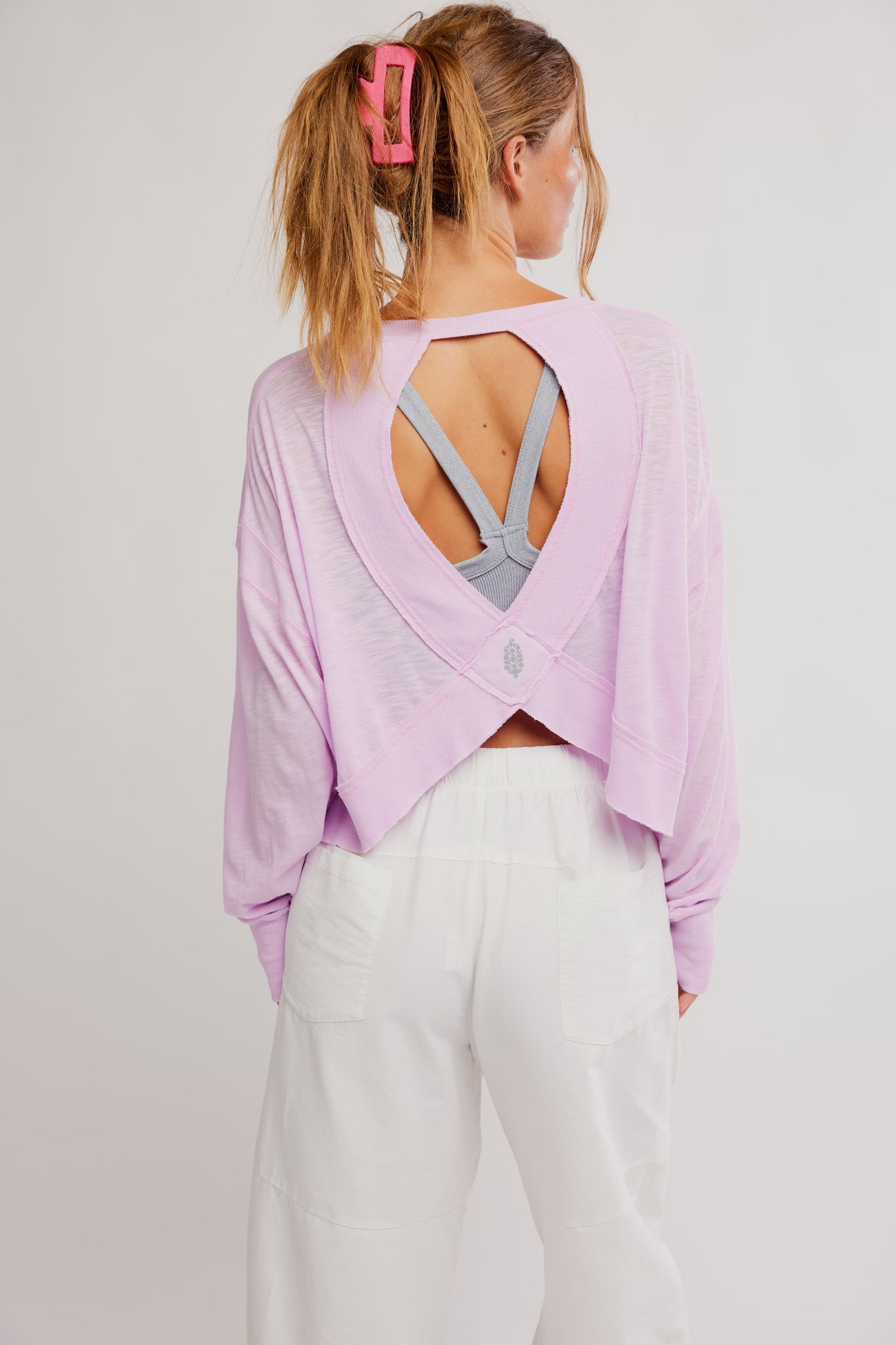 Woman wearing a light purple open-back top and white pants on a plain background