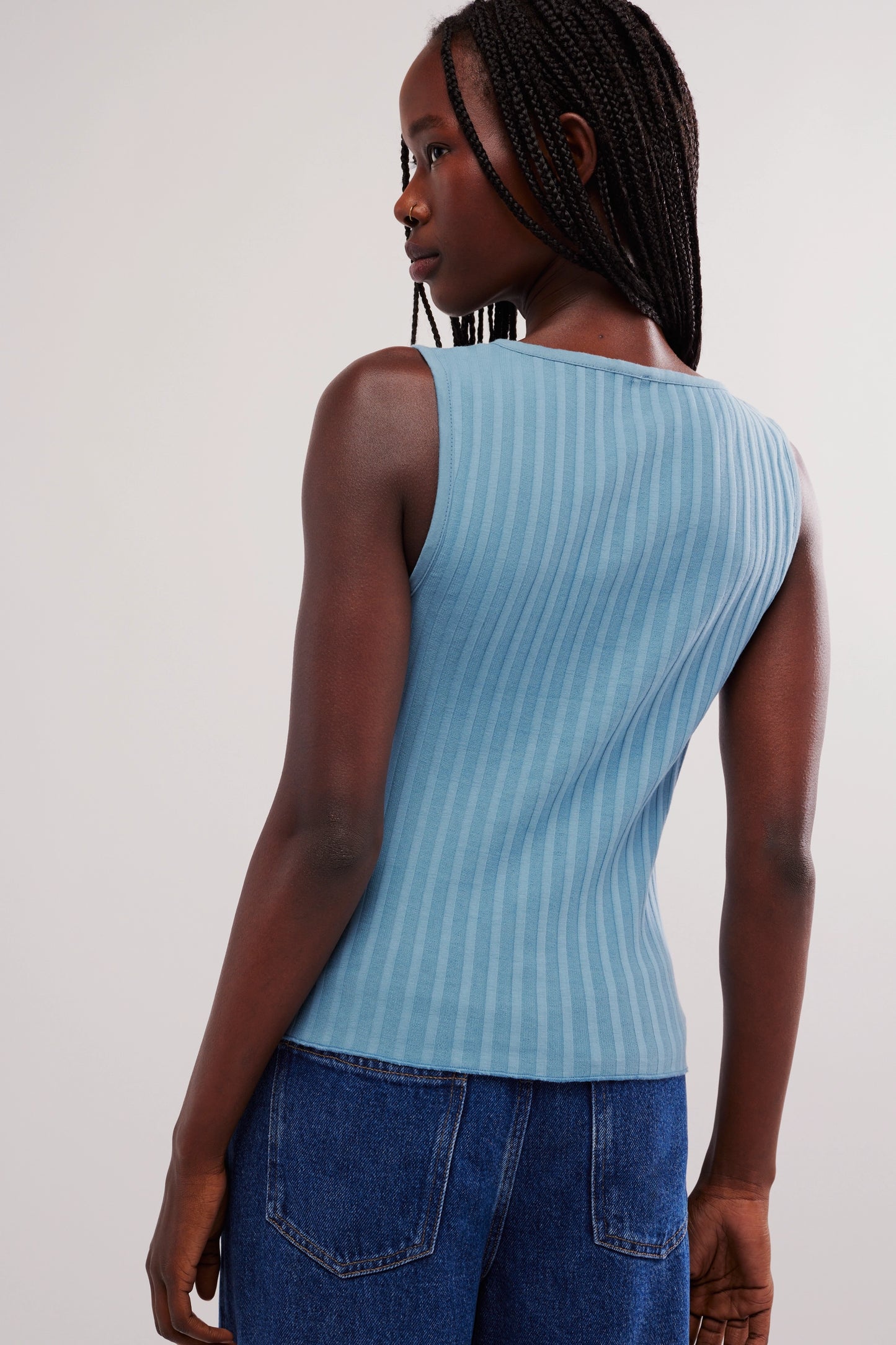 Person wearing a light blue sleeveless top and blue jeans on a white background