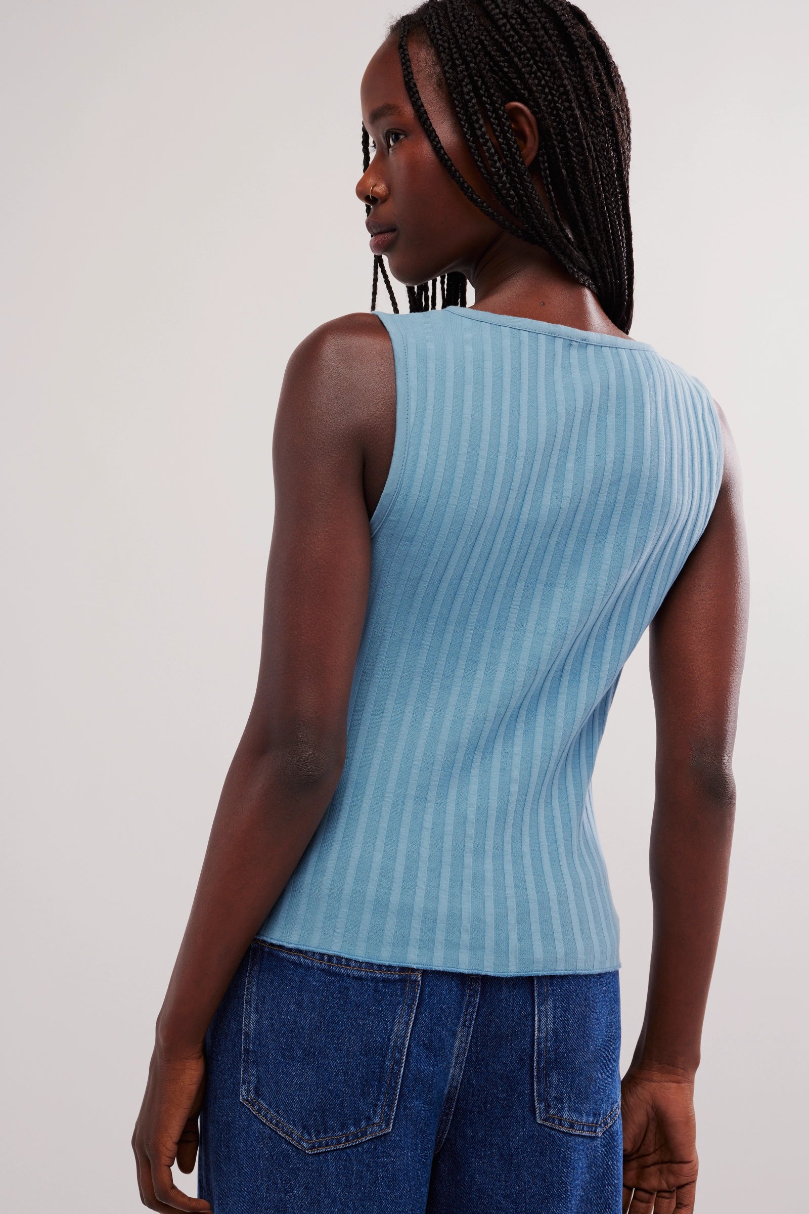 Person wearing a light blue sleeveless top and blue jeans on a white background
