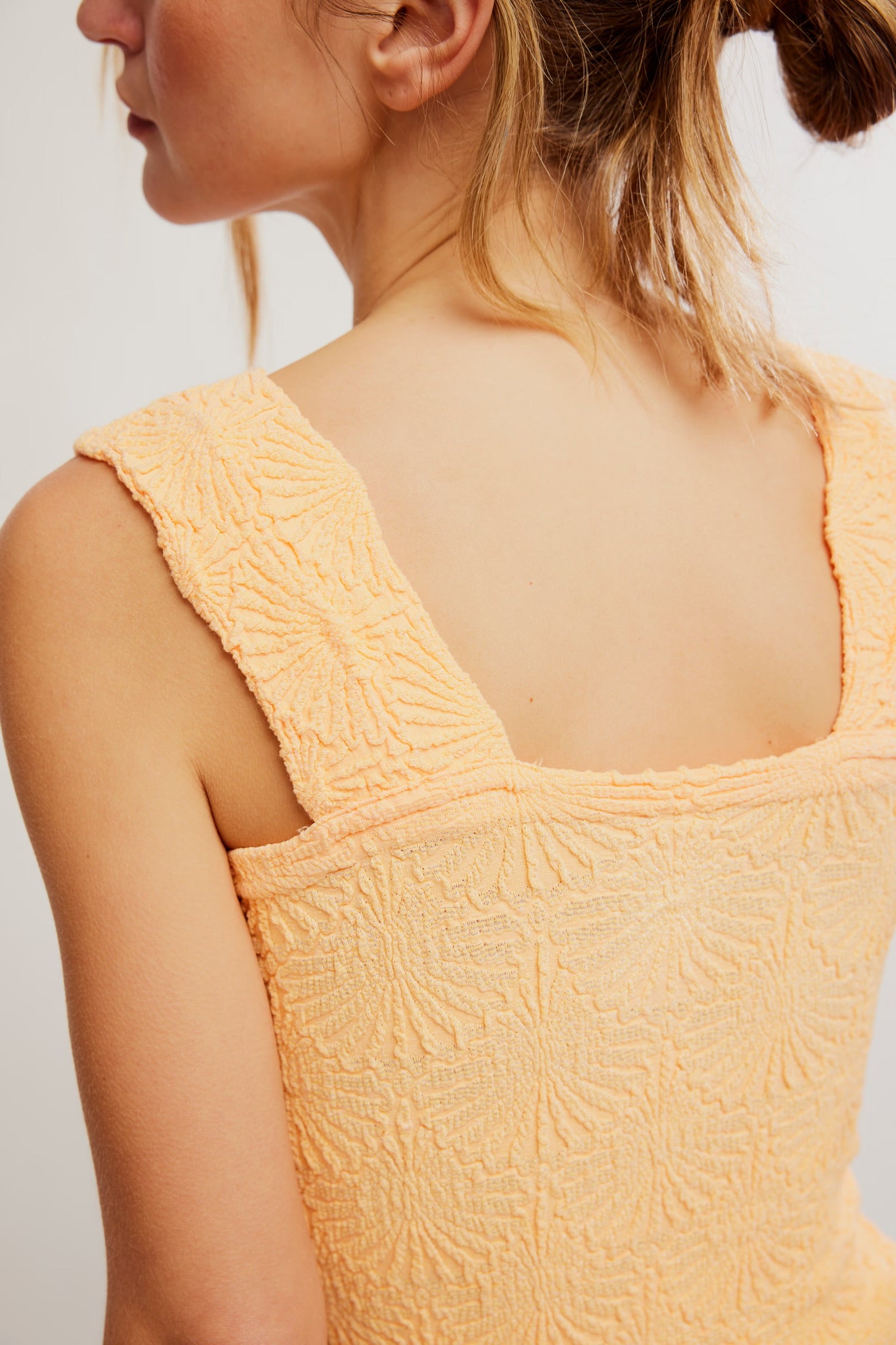 Yellow textured sleeveless top worn by a person on a light background