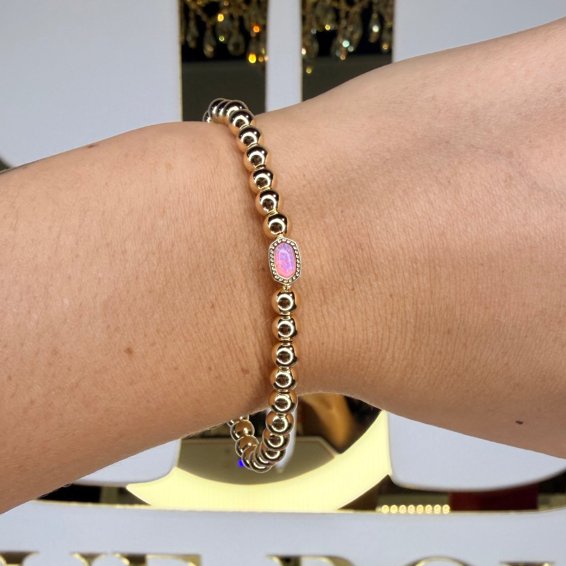 Gold bracelet with pink gemstone on a wrist, blurred background with decorative elements