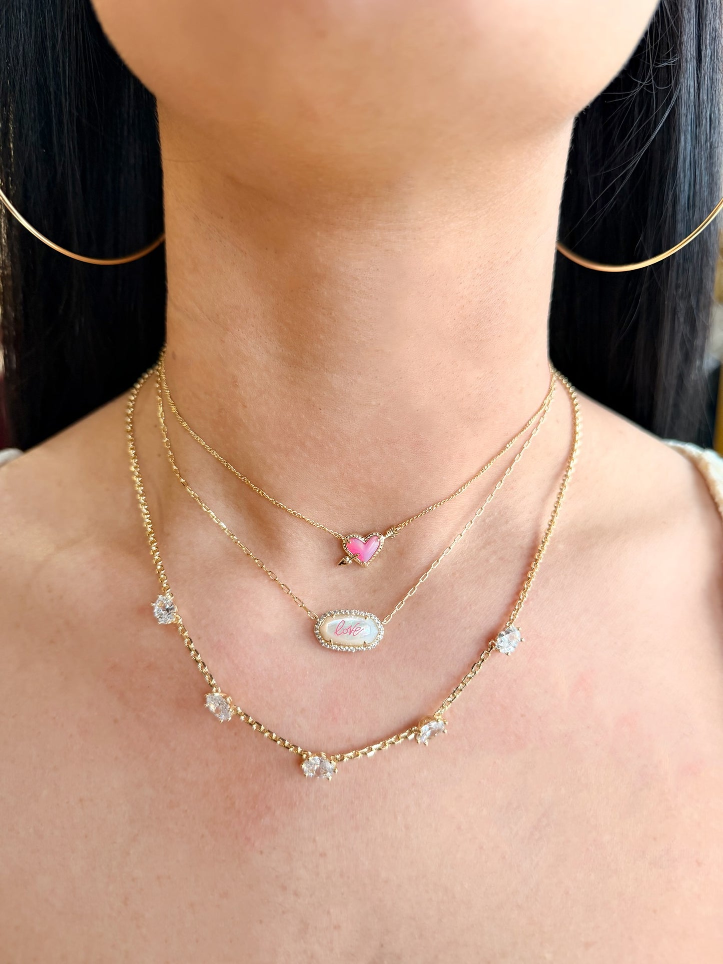 Close-up of a person wearing multiple gold necklaces with heart and opal pendants.