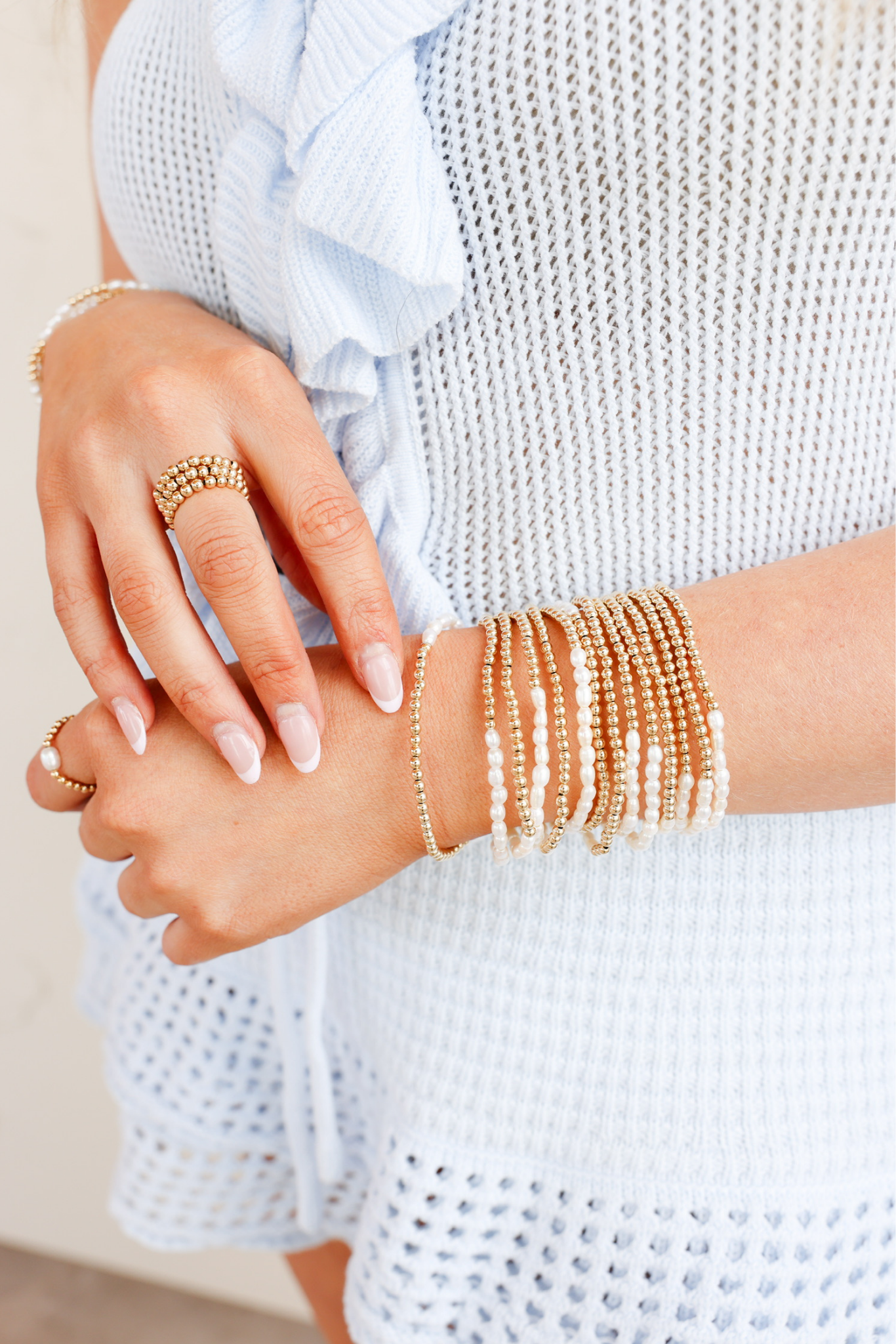 Close-up of a person's hand wearing gold bracelets and rings on a light background