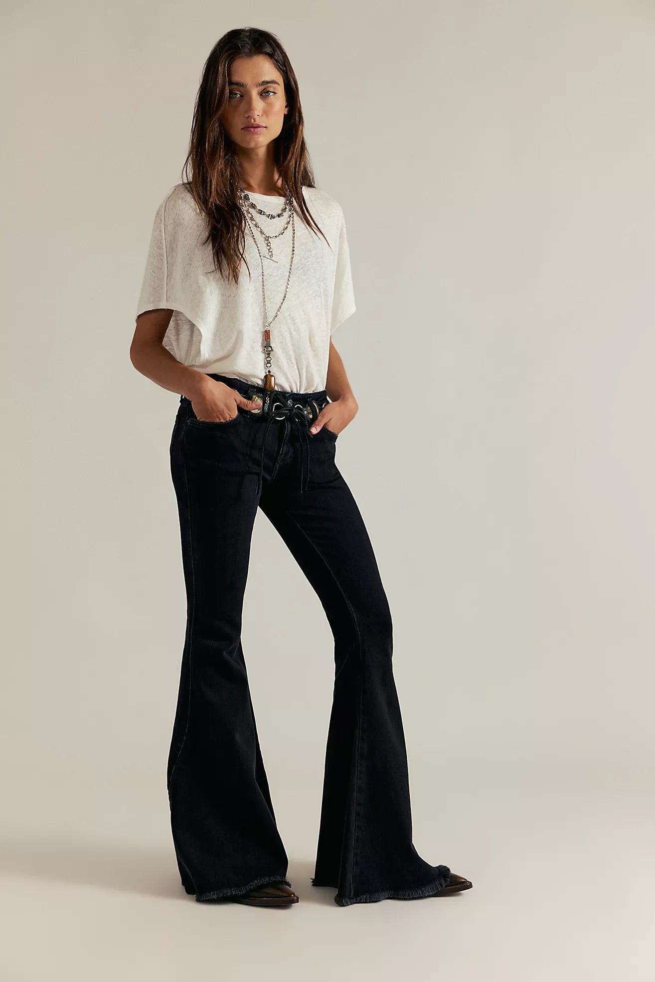 Woman wearing a white top and black flared jeans on a plain background