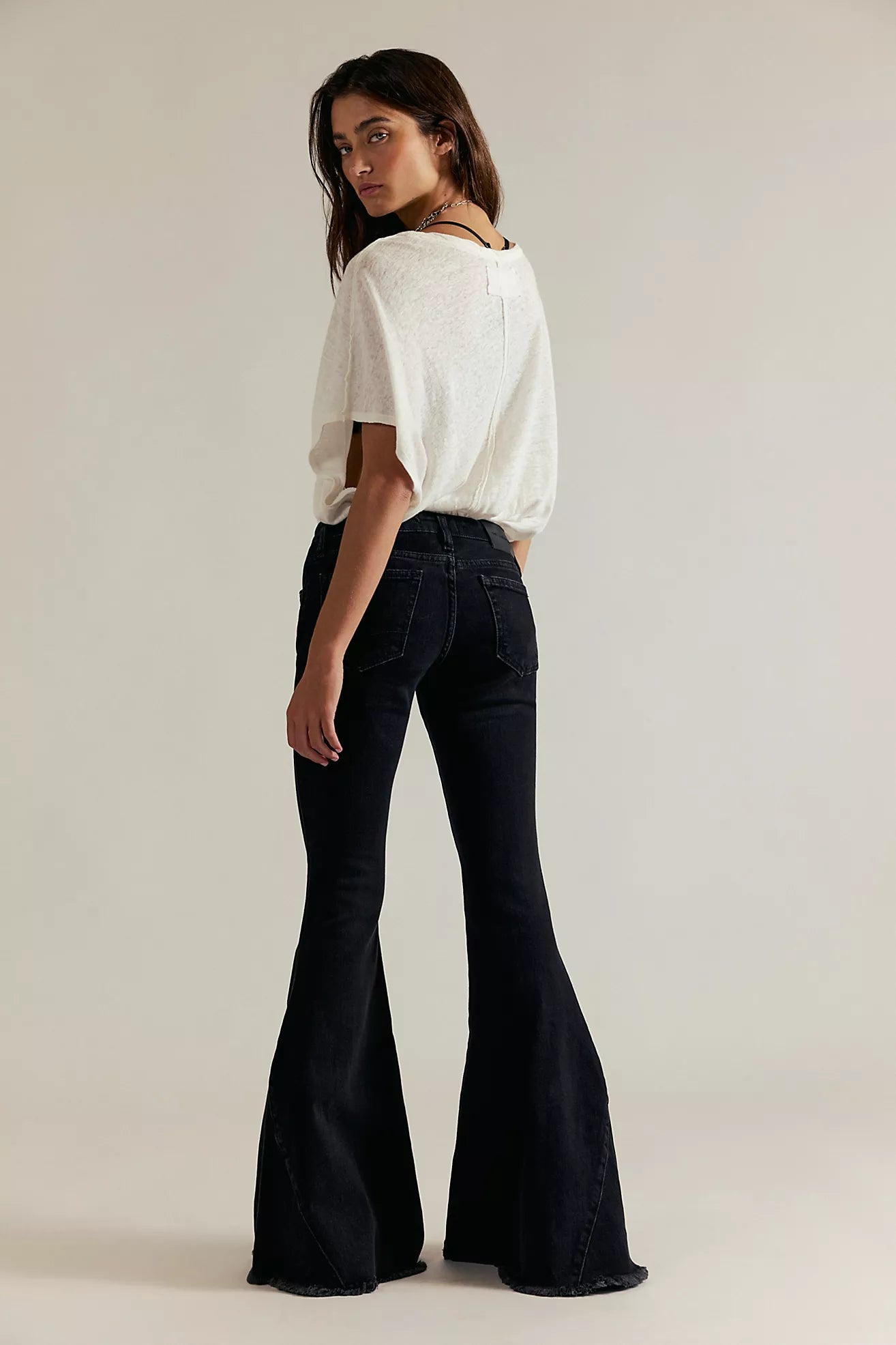 Woman wearing a white top and black flared jeans on a plain background