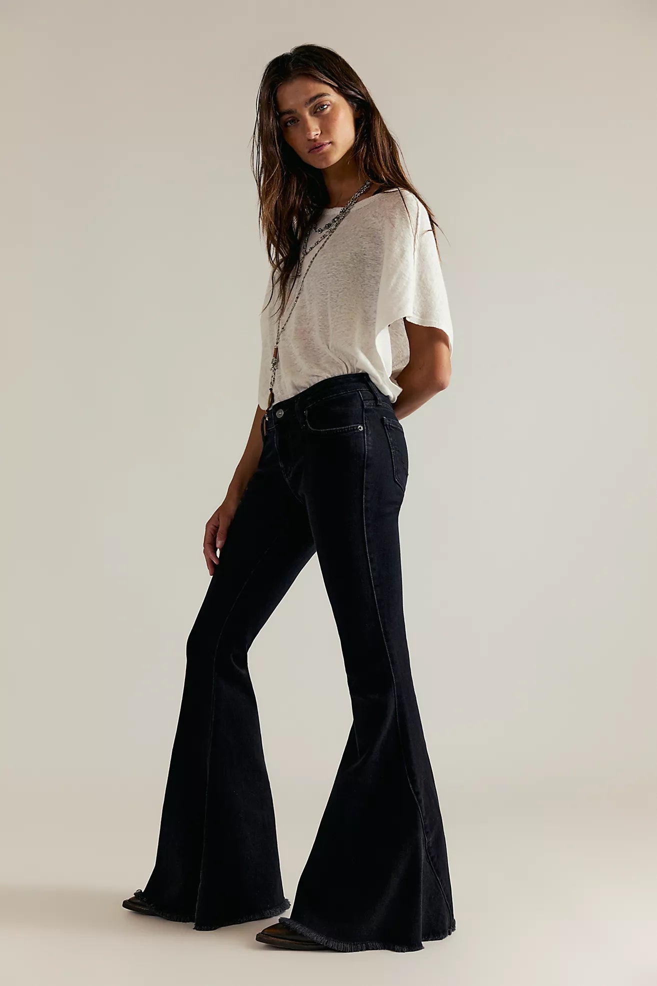 Woman wearing a white top and black flared jeans on a plain background