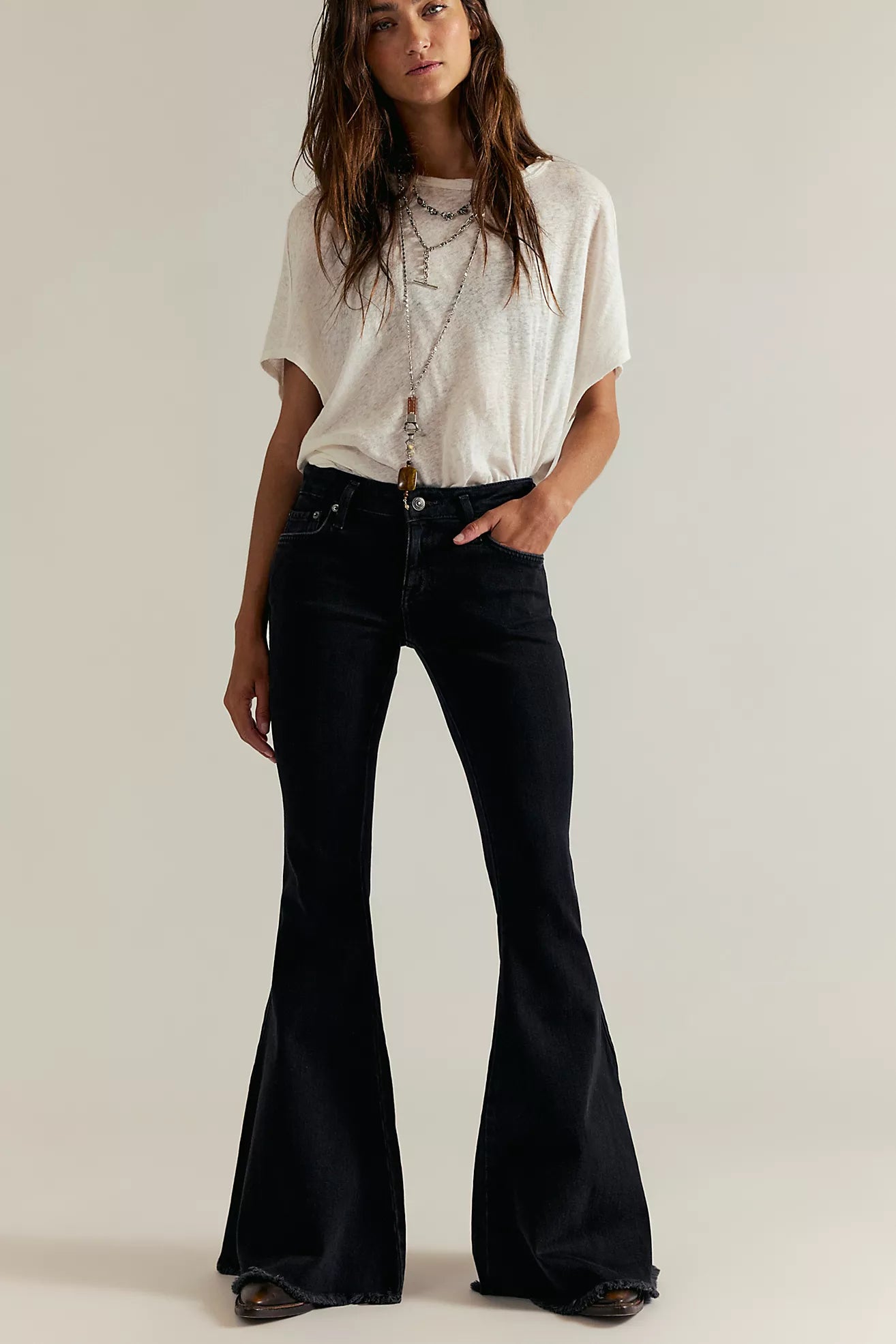 Woman wearing a white top and black flared jeans on a plain background