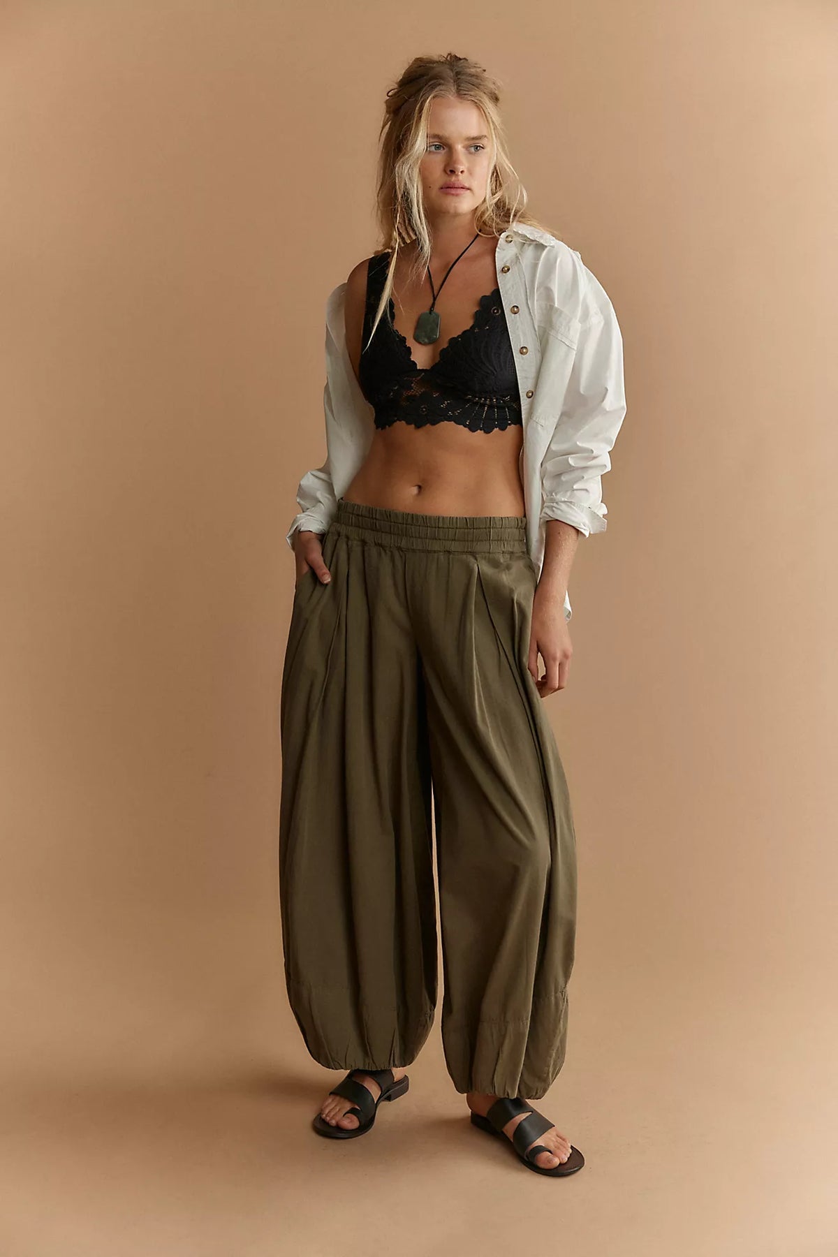 Woman wearing a black bralette, beige jacket, and olive green pants on a beige background